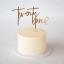 A gold-colored cake topper spelling "twenty one" in a large, elegant script font, placed vertically on top of a plain cream-colored round buttercream cake.