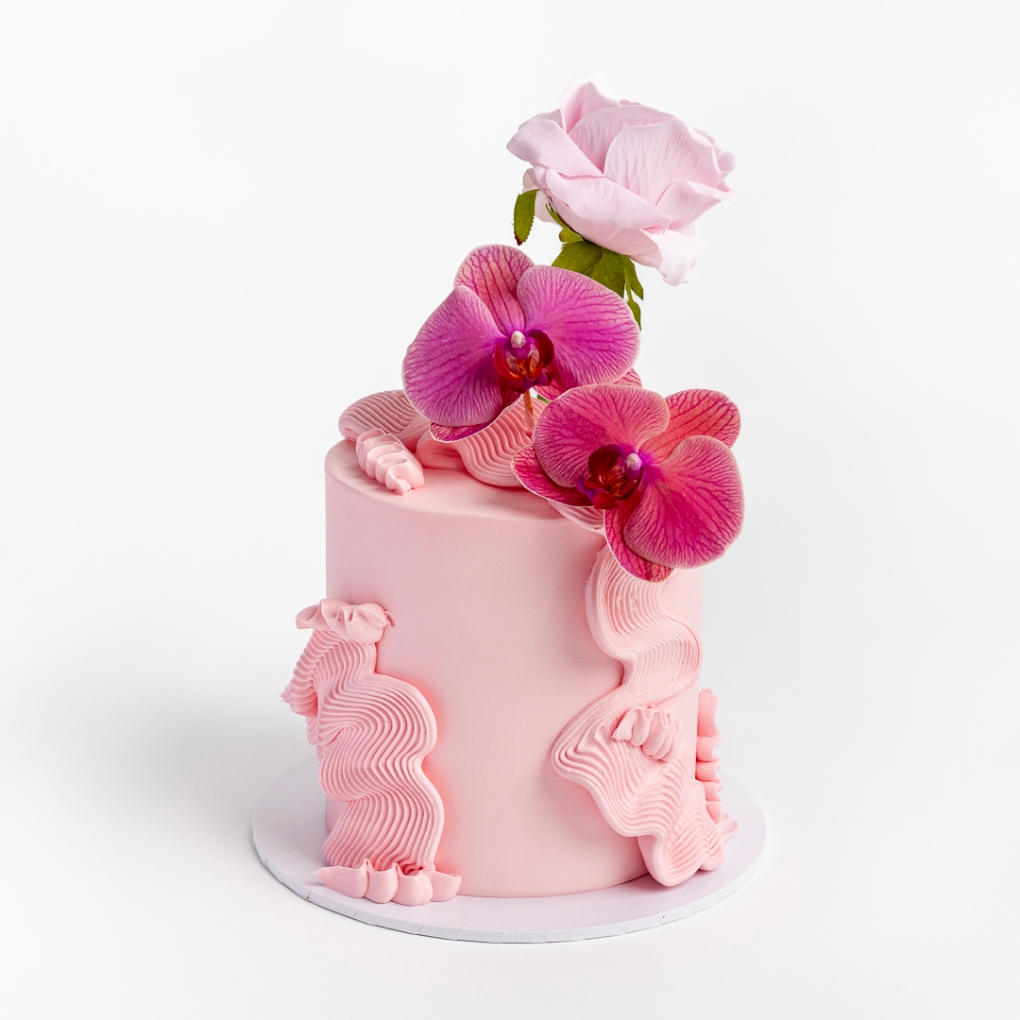 Pink buttercream cake with wavy textured design, topped with fuchsia orchids and a pink rose.